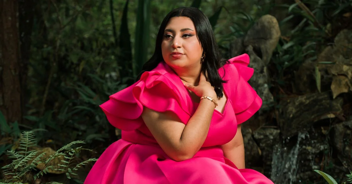 Une femme en robe rose éclatante pose gracieusement au milieu d'un feuillage forestier luxuriant.