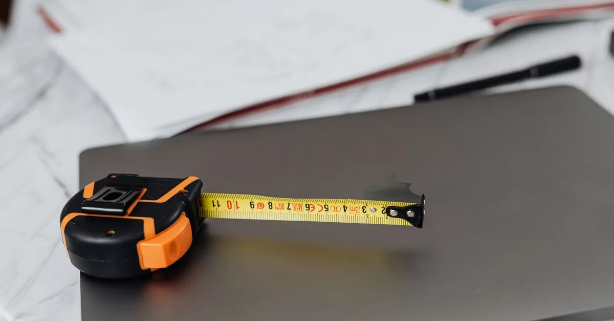 Image en gros plan d'un mètre ruban et d'un ordinateur portable sur un bureau de travail, représentant la précision au travail.