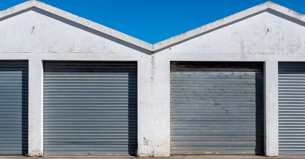 Image de portes de garage industrielles en tôle ondulée sous un ciel bleu clair, illustrant un style architectural minimaliste.