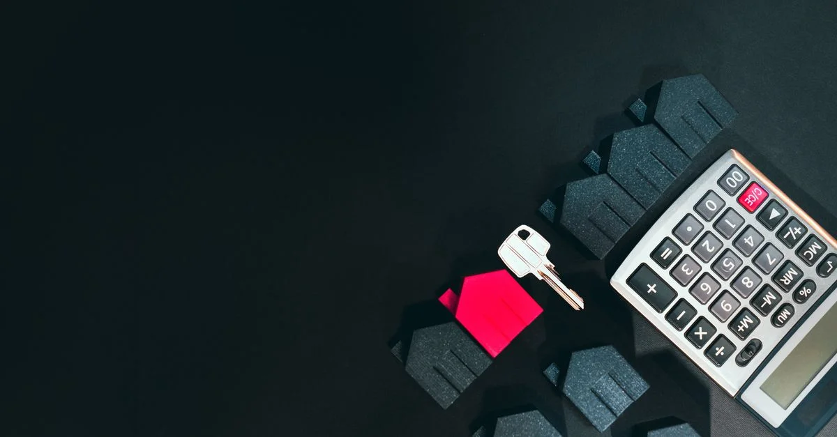 Image conceptuelle de l'immobilier mettant en avant une calculatrice, des maisons, et une clé sur fond noir.
