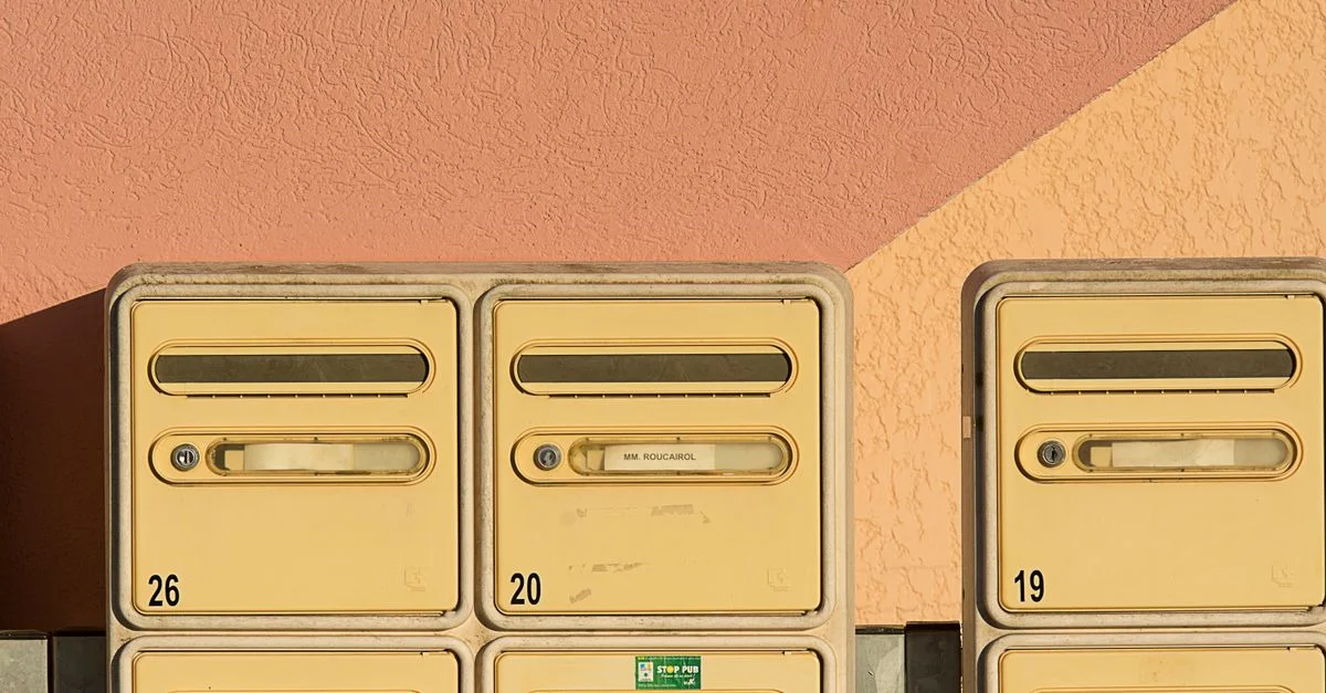 Gros plan sur des boîtes aux lettres jaunes contre un mur rose texturé avec des numéros visibles.