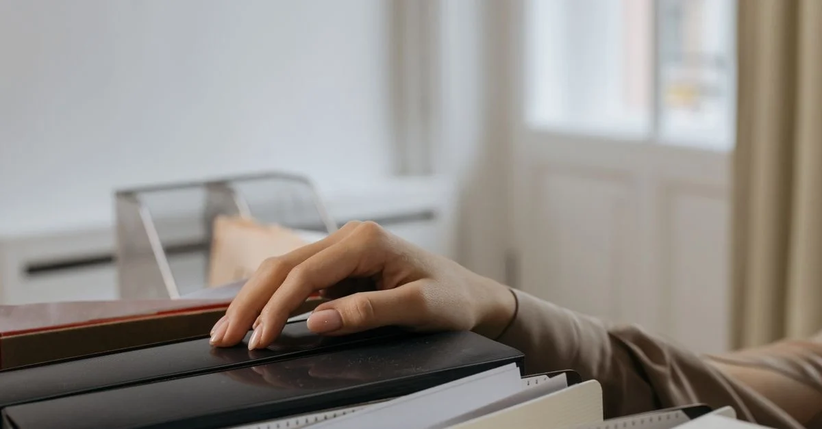 La main d'un adulte atteint des dossiers de bureau, capturant un moment de réflexion. En intérieur.