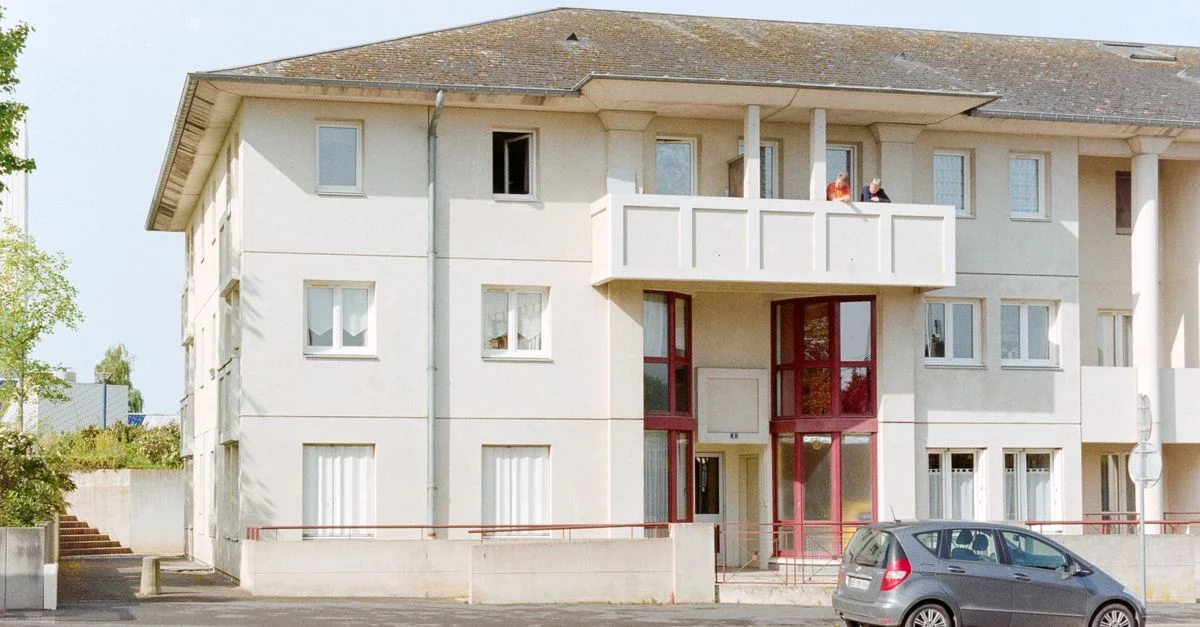 Immeuble résidentiel moderne avec balcons et voiture garée en milieu urbain.