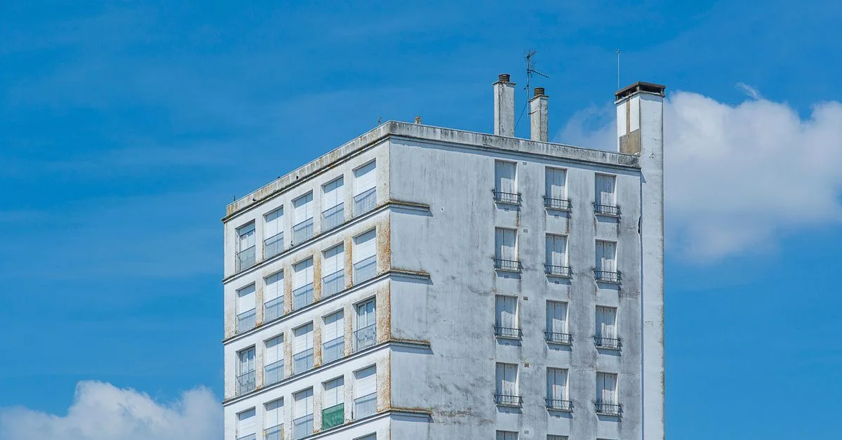Façade d'un immeuble d'appartements urbains modernes contre un ciel bleu vif avec quelques nuages.