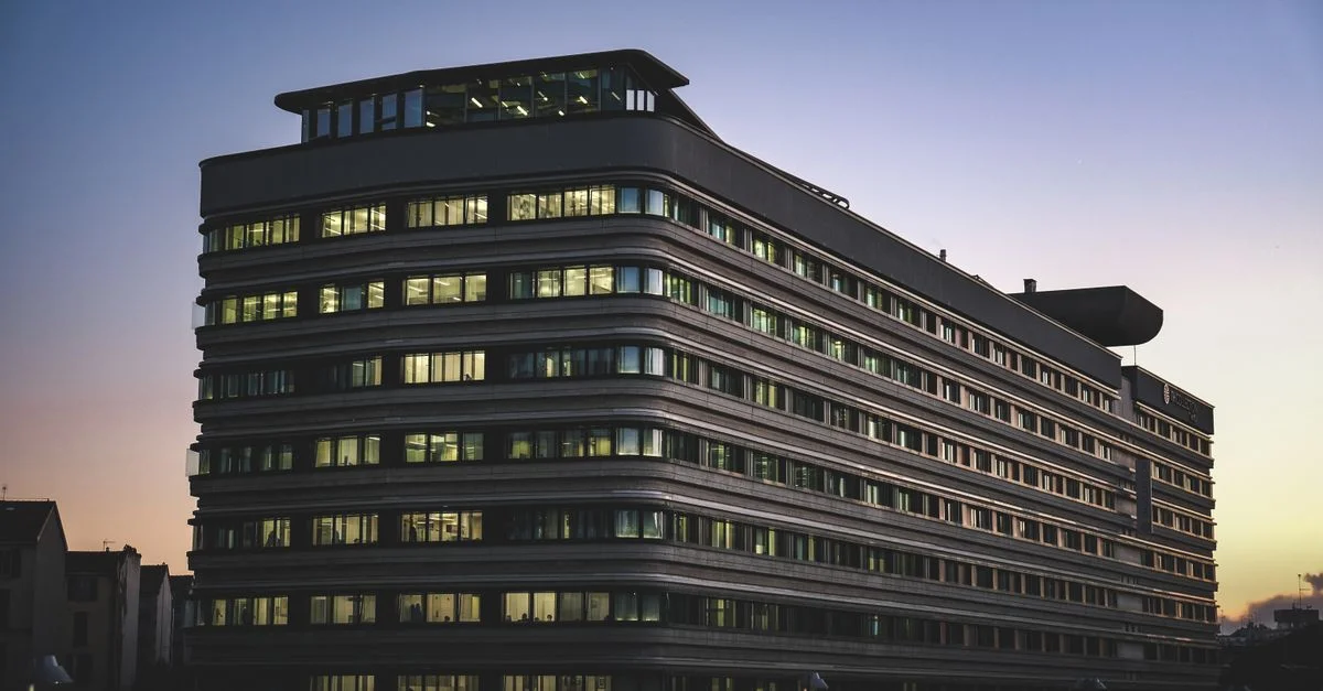 Un bâtiment de bureau moderne magnifiquement illuminé contre le ciel crépusculaire dans un environnement urbain.