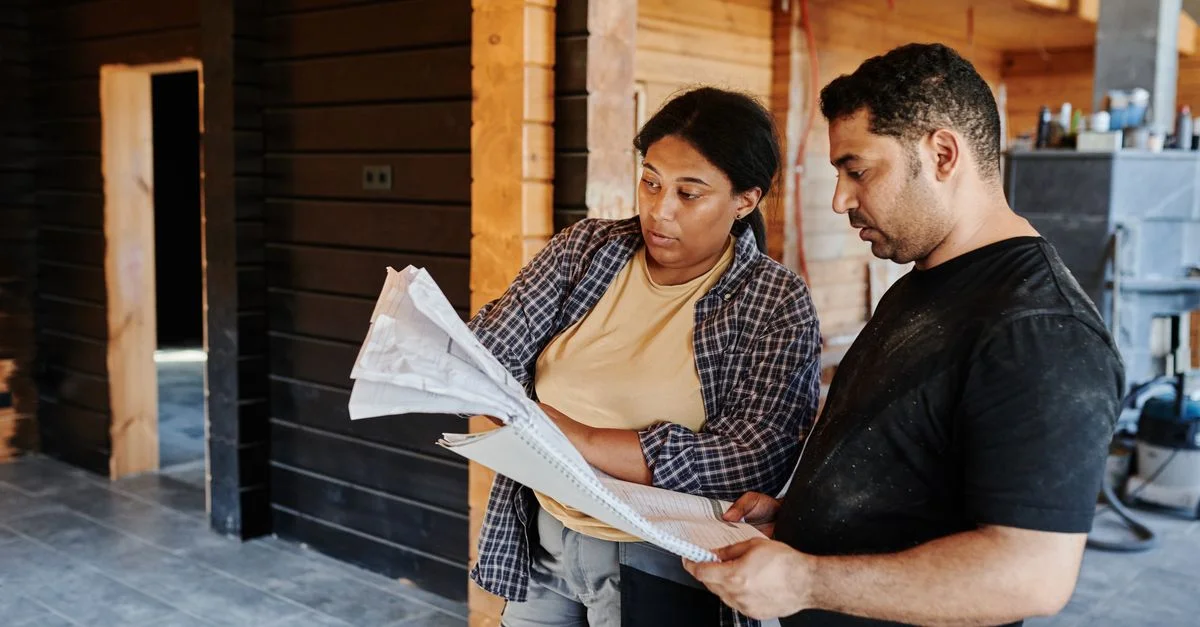 Deux ouvriers du bâtiment examinent des plans à l'intérieur d'une structure en bois, discutant des projets.