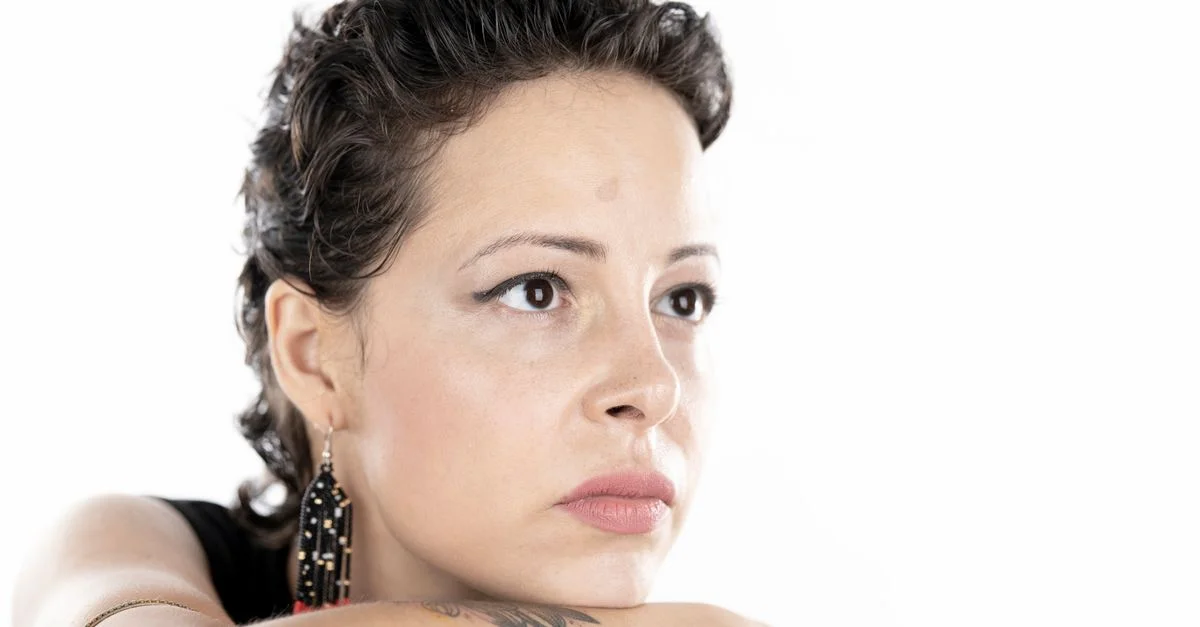 Portrait en gros plan d'une femme pensive avec des tatouages et des boucles d'oreilles, regardant au loin.