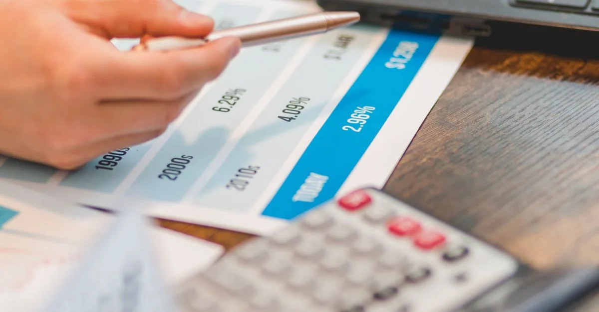 Gros plan d'une main utilisant un stylo à bille et une calculatrice pour analyser les taux d'intérêt sur un graphique.