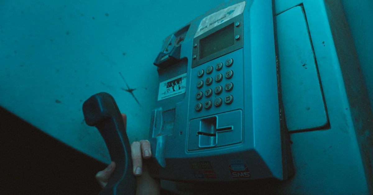 Prise de vue atmosphérique d'une main tenant le combiné d'un téléphone public dans une cabine téléphonique faiblement éclairée.