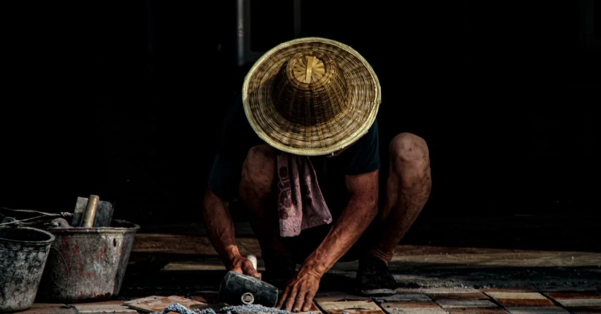 Un maçon installant des carreaux en extérieur, portant un chapeau traditionnel. Focus sur l'artisanat.