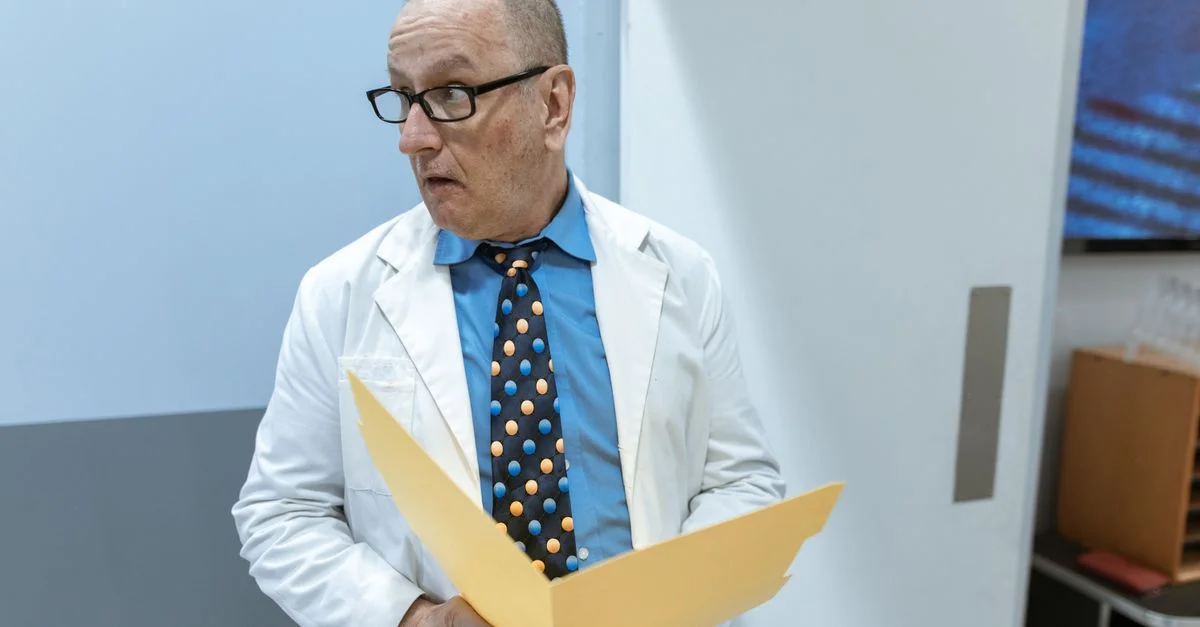 Un médecin senior portant des lunettes examine un dossier dans un couloir d'hôpital.