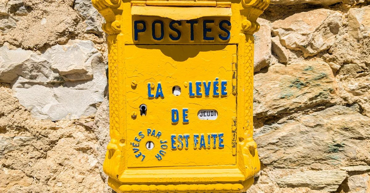 Boîte aux lettres française jaune classique sur un mur de pierre au soleil, parfaite pour les voyages ou les thèmes historiques.