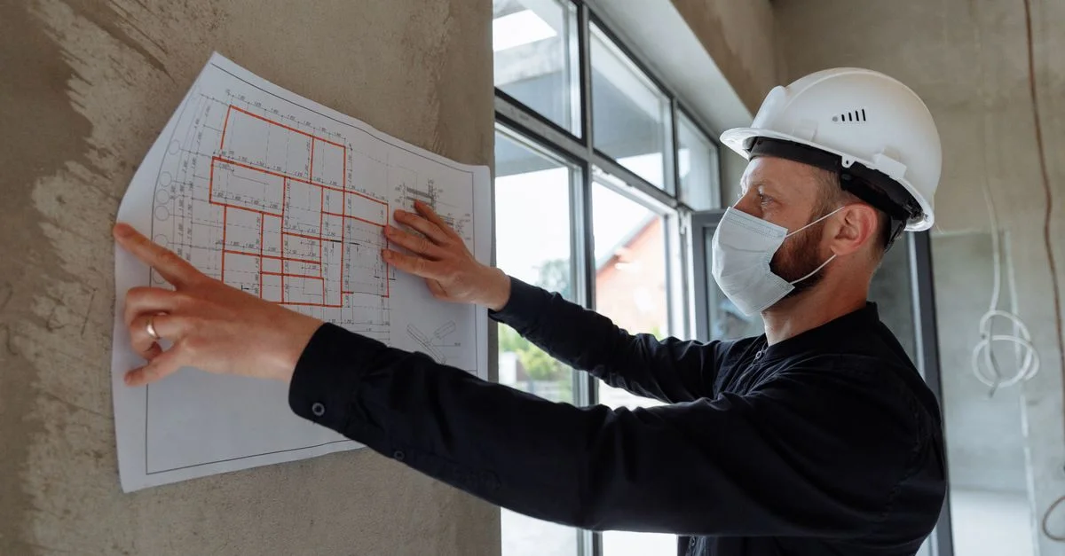 Un architecte portant un casque et un masque examine des plans d'étage sur le site d'un nouveau projet de construction.