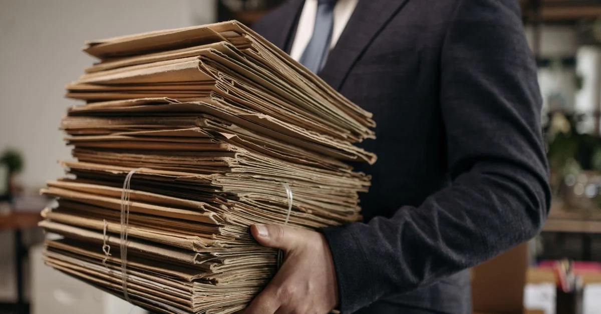 Gros plan d'un professionnel d'affaires tenant une grande pile de dossiers marron dans un cadre de bureau.