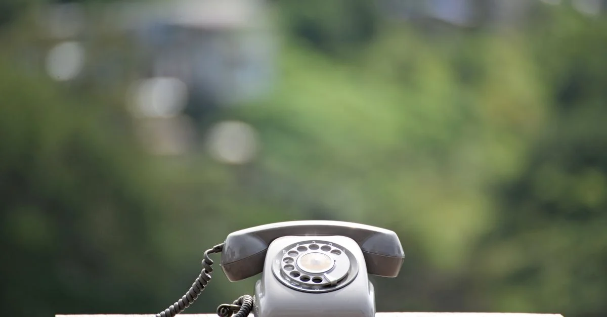 Un téléphone à cadran rotatif classique placé sur une surface en bois avec un fond vert flou.