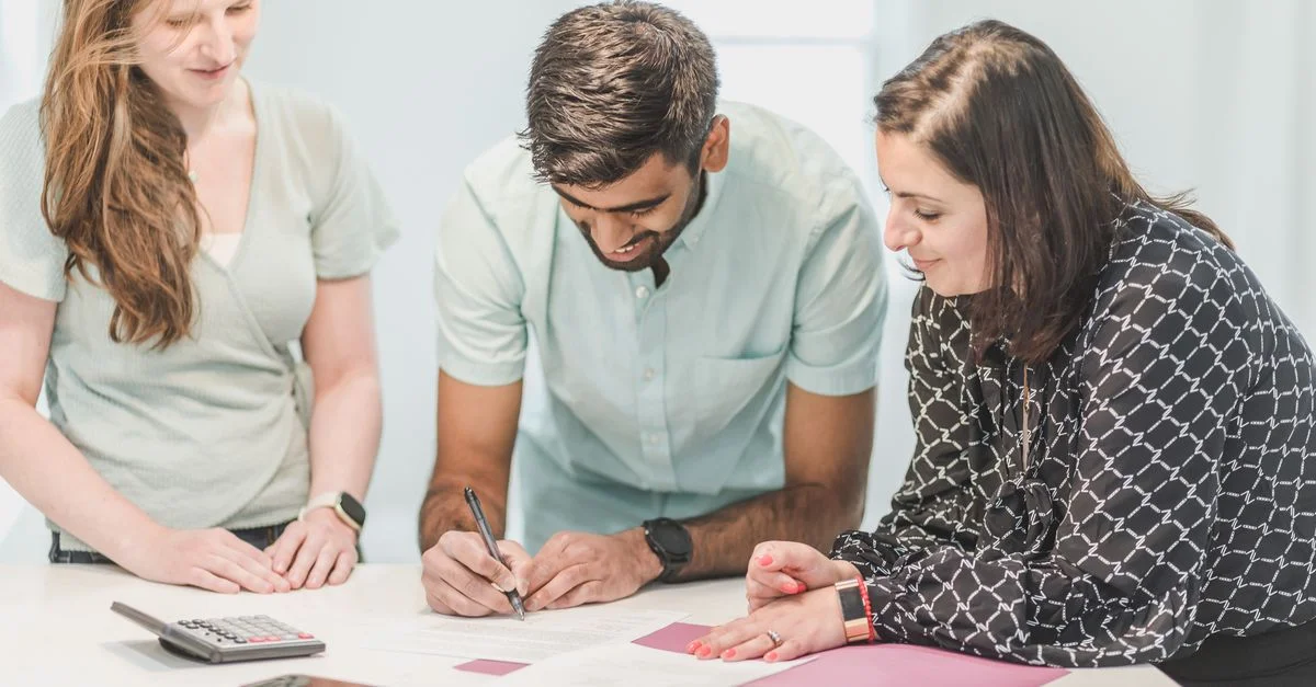 Trois adultes examinant et signant des documents immobiliers à l'intérieur.