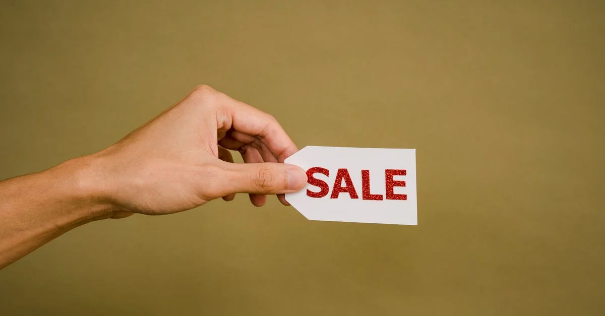 Une main tenant une étiquette 'VENTE' sur un fond marron, idéale pour la promotion commerciale.