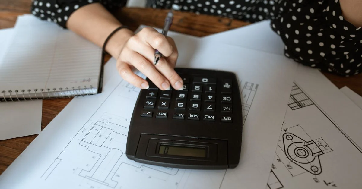 Gros plan sur la main d'un architecte utilisant une calculatrice sur des plans techniques avec une chemise à pois.