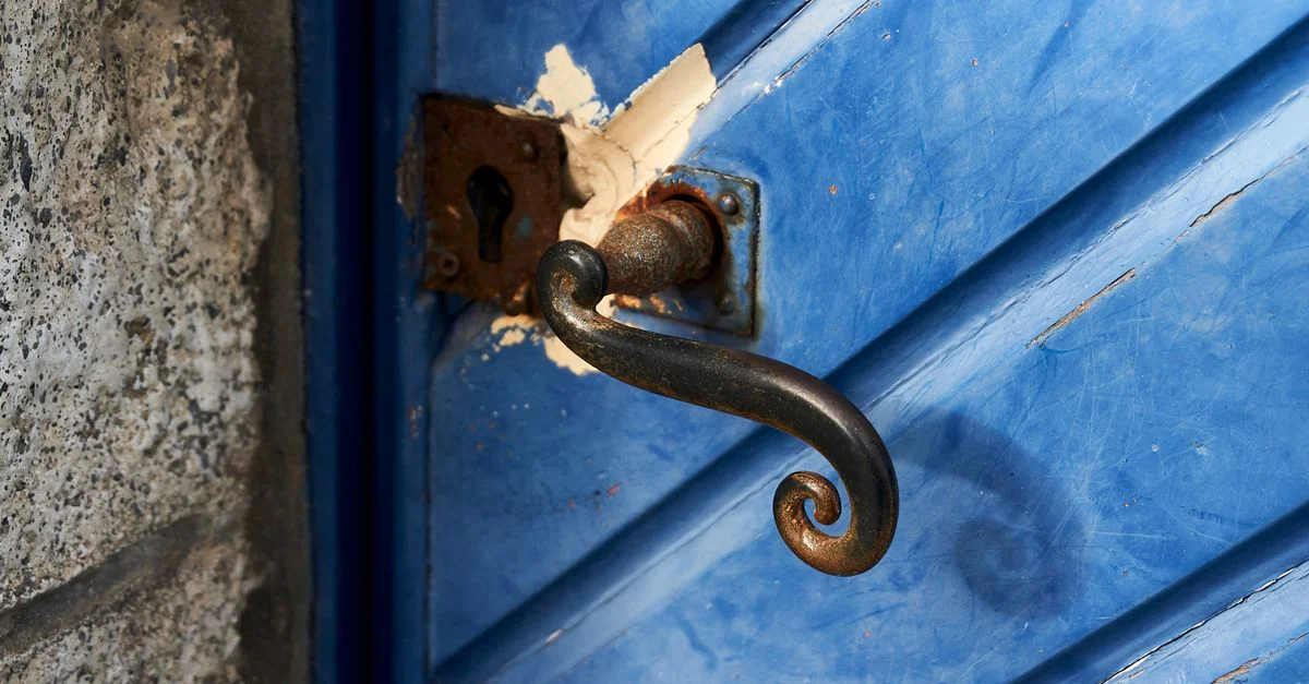 Une vue détaillée d'une porte en bois bleu vieillie avec une poignée en fer rustique et des signes d'usure.