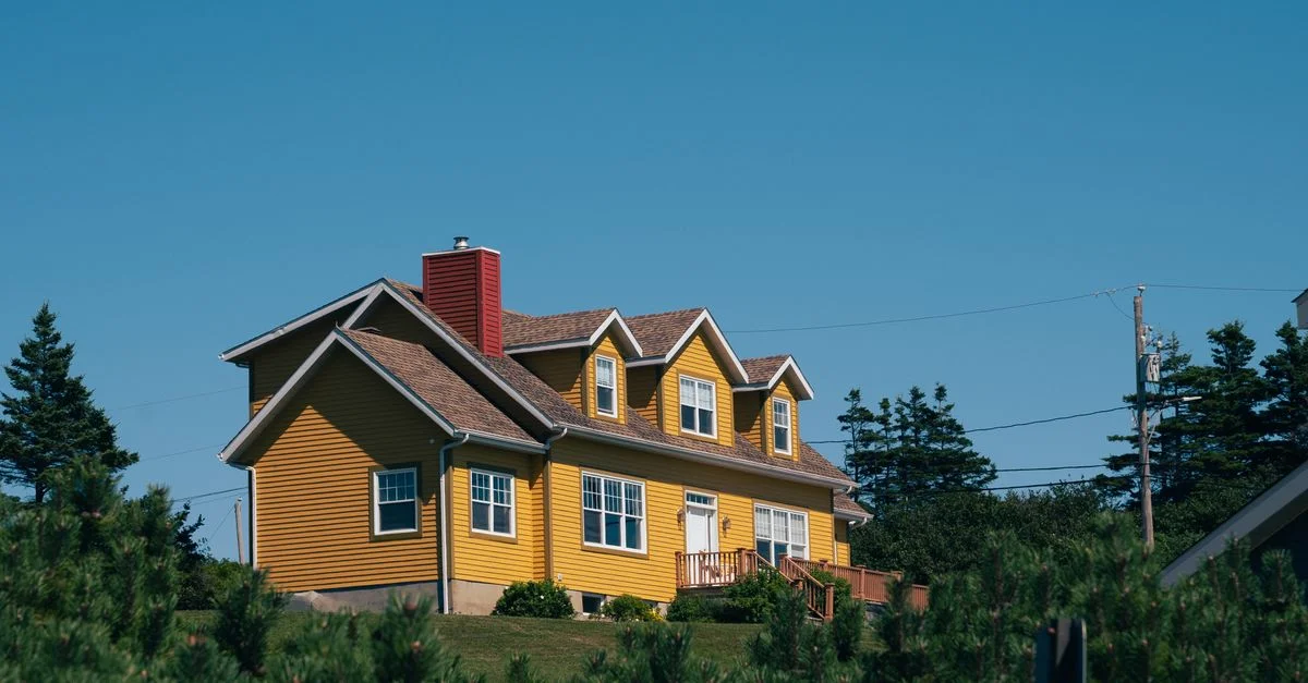 Une maison jaune éclatante nichée dans la campagne de Percé, QC, Canada, entourée d'une végétation luxuriante.
