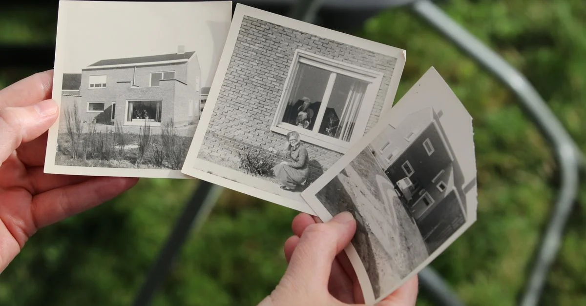 Mains tenant des photos vintage en noir et blanc de vieilles maisons à l'extérieur.