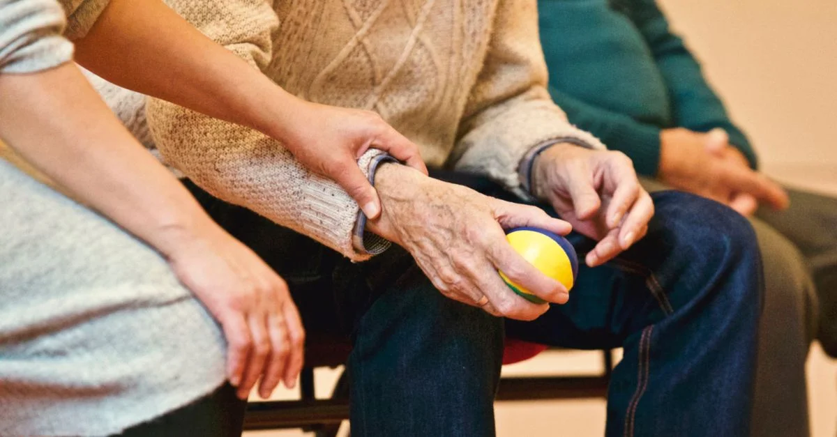 Une personne âgée reçoit de l'aide d'un soignant, tenant des mains à l'intérieur, montrant de la compassion.